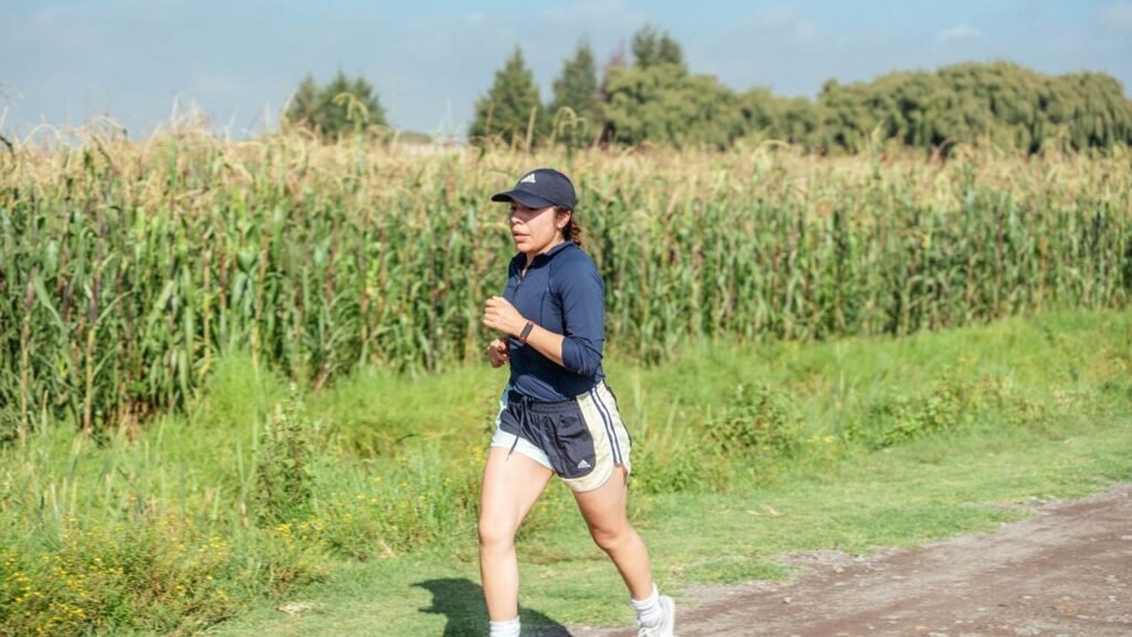 Woman jogging along a rural path next to a cornfield, enjoying fitness in nature.